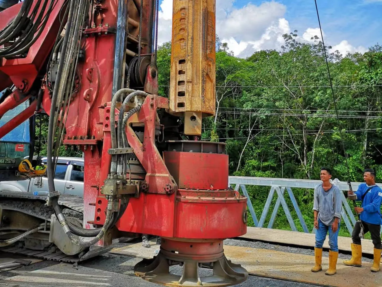 Bored piling rig lifting its drilling tool on a bridge site, with two crew watching